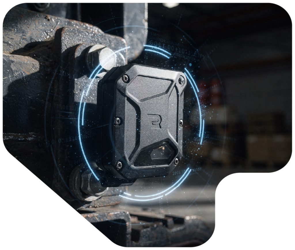 Close‑up of a rugged black industrial sensor mounted on heavy machinery, with a stylized ‘R’ logo on its front panel, surrounded by a glowing circular digital interface of blue and white elements, in a warehouse setting with shelves and boxes in the background.