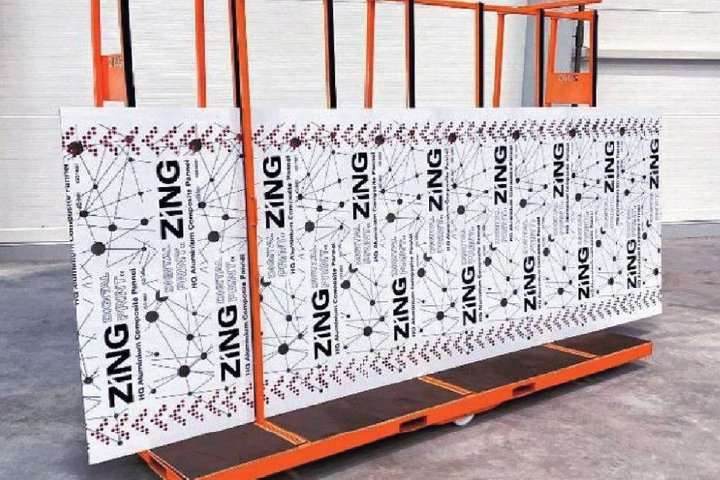 Stack of aluminum composite panels branded Zing placed on orange metal cart panels printed with black dot and line design resembling molecular network text indicating HQ aluminum composite panel digital surface mineral core A2 class fireproof used for construction and architectural applications.